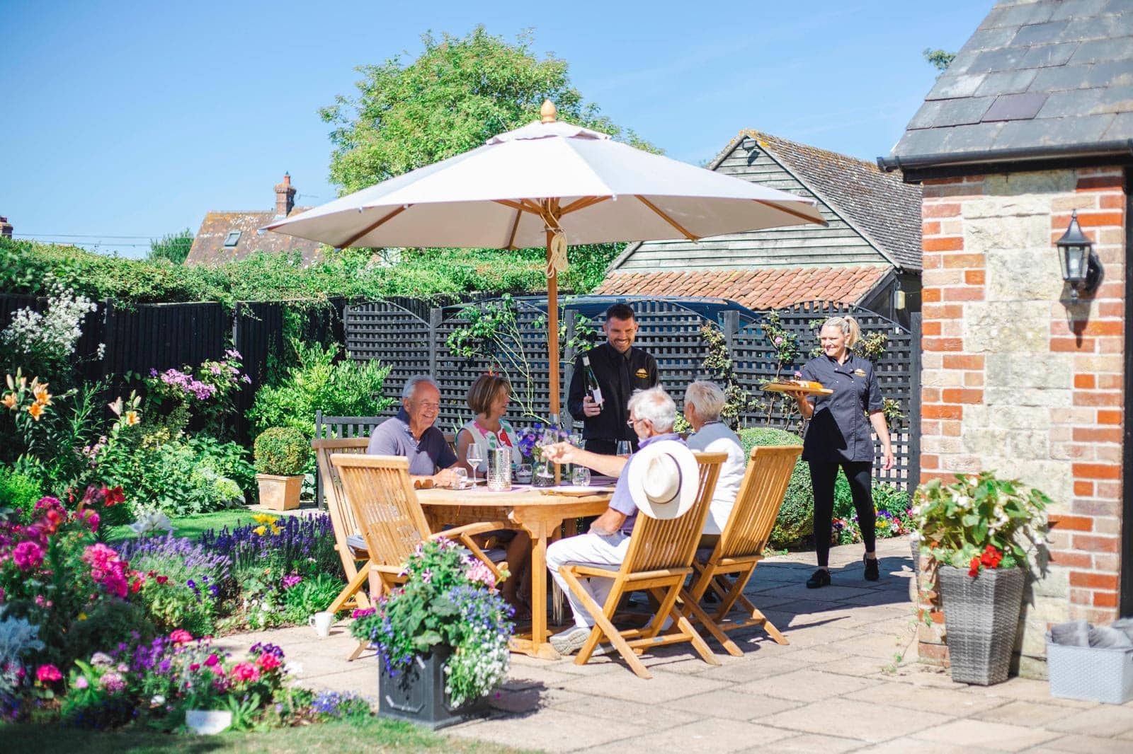 Photo of English Cottage Vacation hosts Laura and Nathan serving guests in the garden at Well Cottage